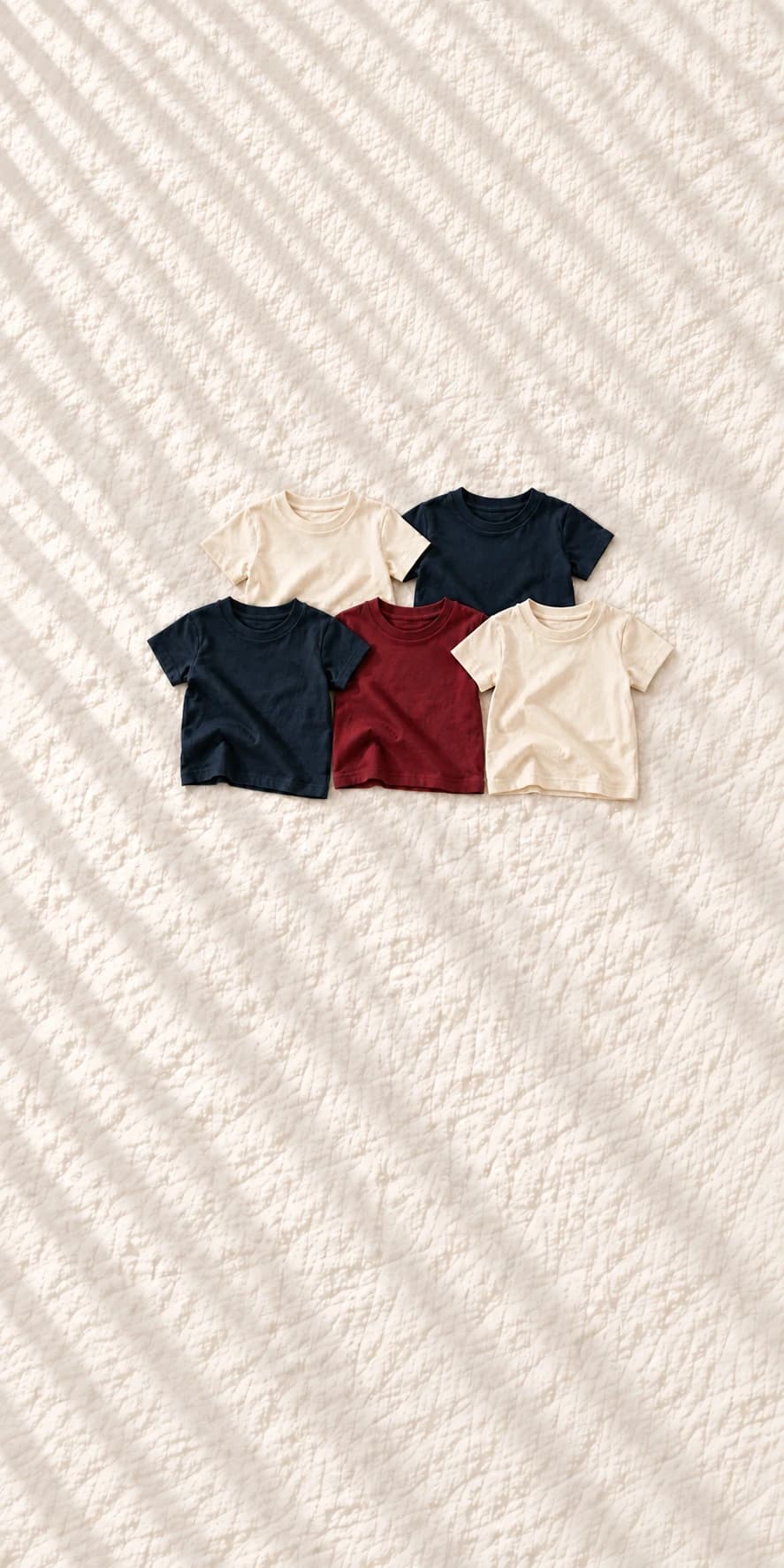 Cinque T-shirt bambino Farway, panna, blu e bordeaux, disposte su lino chiaro